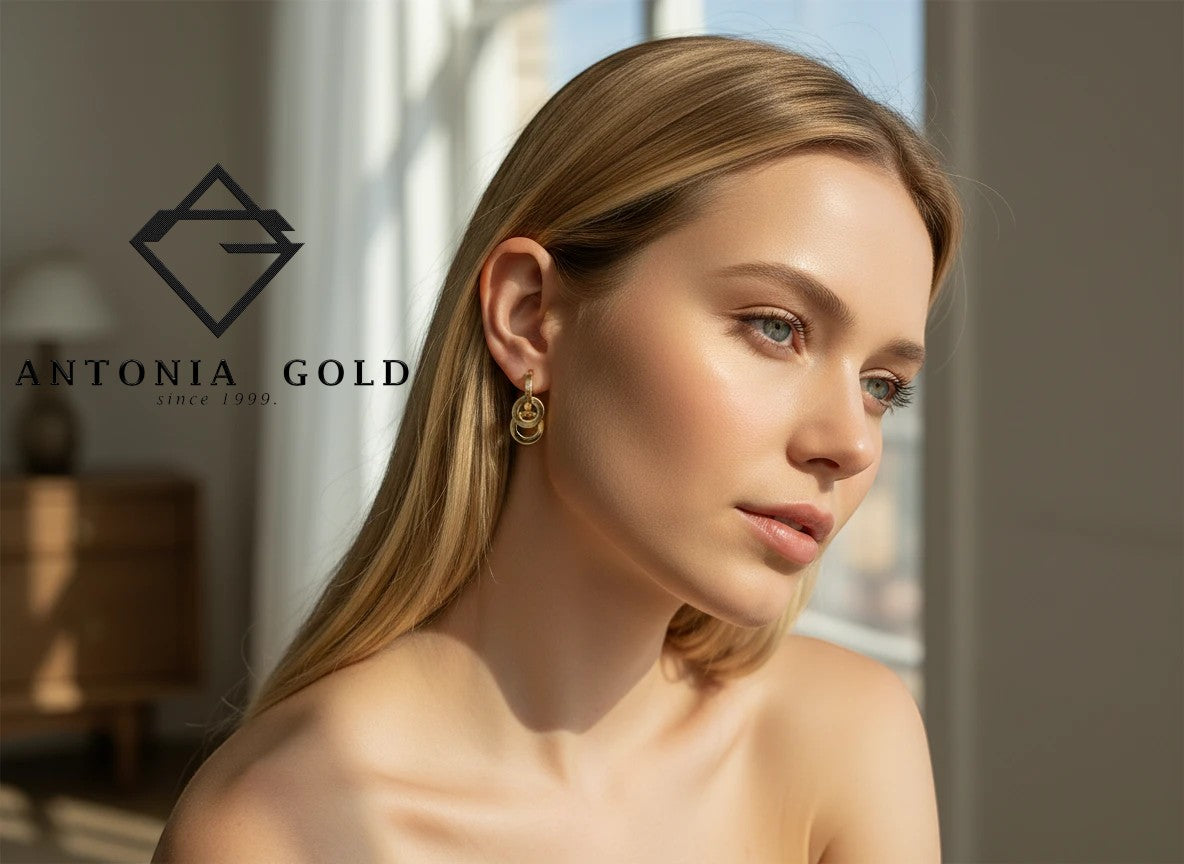 Cercei Antonia Gold tip hoop din aur cu elemente rotunde mobile purtați de o femeie cu păr blond lângă o fereastră