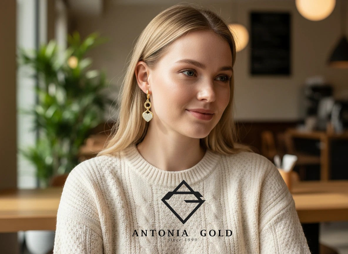 Femeie blondă purtând cercei Antonia Gold tip verigă din aur cu pandantiv în formă de inimă decorat cu pietre strălucitoare