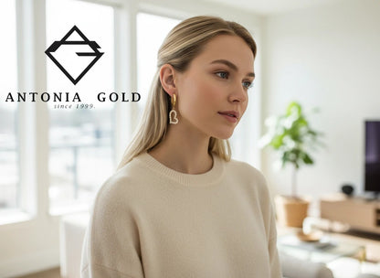 Cercei Antonia Gold tip creole din aur galben cu pandantiv inimă decorat cu pietre albe purtați de o tânără blondă